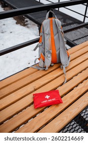 A sturdy backpack can be seen resting on a wellcrafted wooden bench that is placed beside a first aid kit, which may offer assistance in case of any emergencies that may arise outdoors