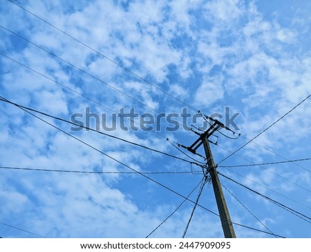 The sturdy electric pole stands under the hot sun against the bright sky 