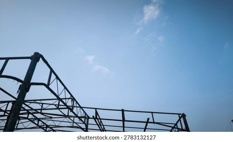 A sturdy metal framework, possibly from a construction site or an old building, stands silhouetted against a vast, clear blue sky, emphasizing industrial architecture.