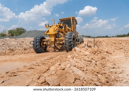 A sturdy motor grader levels the earth under a bright sky. Capturing the raw power and efficiency of heavy machinery in action.