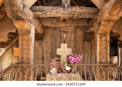 sturdy recycled wooden shrine with two crosses, a stone cross on an altar with flower decorations, protected by a wrought-iron railing.