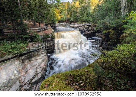 The Sturgeon River flows rapidly over Canyon Falls near L'Anse Michigan. Autumn colors are in the background. Known as Michigans Grand Canyon, an overlook is seen next to the waterfall.