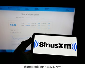 Stuttgart, Germany - 02-13-2022: Person holding mobile phone with logo of US broadcasting company Sirius XM Holdings Inc. on screen in front of web page. Focus on phone display. Unmodified photo.
