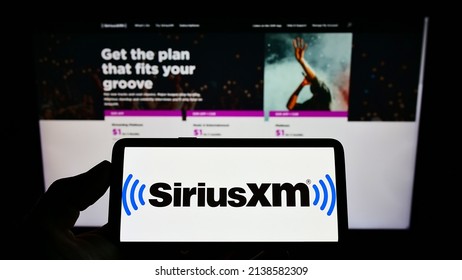 Stuttgart, Germany - 02-13-2022: Person holding smartphone with logo of US broadcasting company Sirius XM Holdings Inc. on screen in front of website. Focus on phone display. Unmodified photo.