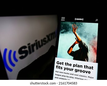Stuttgart, Germany - 02-13-2022: Person holding smartphone with webpage of US broadcasting company Sirius XM Holdings Inc. on screen with logo. Focus on center of phone display. Unmodified photo.