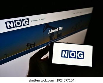 Stuttgart, Germany - 02-16-2021: Person holding mobile phone with logo of American oil company Northern Oil and Gas Inc. (NOG) on screen in front of web page. Focus on phone display. Unmodified photo.