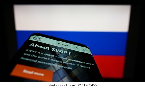 Stuttgart, Germany - 02-27-2022: Person Holding Mobile Phone With Webpage Of Banking Transaction System SWIFT On Screen In Front Of Russian Flag. Focus On Phone Display. Unmodified Photo.