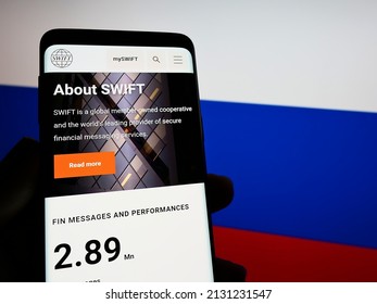 Stuttgart, Germany - 02-27-2022: Person Holding Cellphone With Website Of Banking Transaction System SWIFT On Screen In Front Of Russian Flag. Focus On Phone Display. Unmodified Photo.