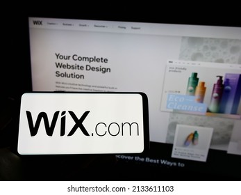 Stuttgart, Germany - 03-01-2022: Person holding mobile phone with logo of Israeli software company Wix.com Ltd. on screen in front of business web page. Focus on phone display. Unmodified photo.