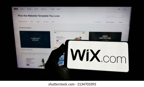 Stuttgart, Germany - 03-01-2022: Person holding cellphone with logo of Israeli software company Wix.com Ltd. on screen in front of business webpage. Focus on phone display. Unmodified photo.