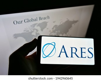 Stuttgart, Germany - 03-13-2021: Person holding mobile phone with logo of US investment company Ares Management Corporation on screen in front of website. Focus on cellphone display. Unmodified photo.