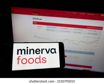 Stuttgart, Germany - 03-30-2022: Person holding mobile phone with logo of Brazilian foods company Minerva SA on screen in front of business web page. Focus on phone display. Unmodified photo.
