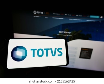 Stuttgart, Germany - 05-08-2022: Person holding smartphone with logo of Brazilian software company TOTVS S.A. on screen in front of website. Focus on phone display. Unmodified photo.
