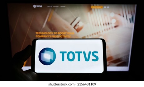 Stuttgart, Germany - 05-08-2022: Person holding cellphone with logo of Brazilian software company TOTVS SA on screen in front of business webpage. Focus on phone display. Unmodified photo.