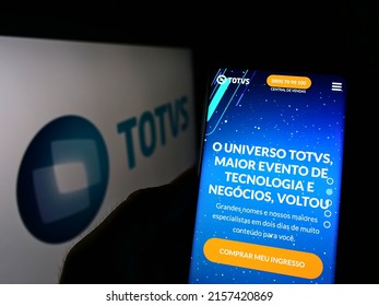 Stuttgart, Germany - 05-08-2022: Person holding cellphone with website of Brazilian software company TOTVS SA on screen in front of logo. Focus on center of phone display. Unmodified photo.