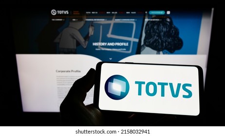 Stuttgart, Germany - 05-08-2022: Person holding mobile phone with logo of Brazilian software company TOTVS S.A. on screen in front of business web page. Focus on phone display. Unmodified photo.