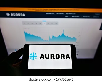 Stuttgart, Germany - 05-22-2021: Person holding smartphone with logo of Canadian company Aurora Cannabis Inc. on screen in front of website. Focus on phone display. Unmodified photo.