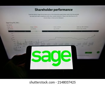 Stuttgart, Germany - 05-22-2021: Person holding mobile phone with business logo of British software company The Sage Group plc on screen in front of webpage. Focus on phone display. Unmodified photo.