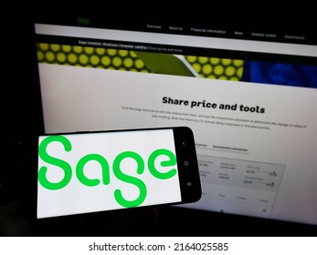 Stuttgart, Germany - 05-29-2022: Person holding mobile phone with logo of British software company The Sage Group plc on screen in front of web page. Focus on phone display. Unmodified photo.