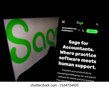 Stuttgart, Germany - 05-29-2022: Person holding cellphone with webpage of British software company The Sage Group plc on screen in front of logo. Focus on center of phone display. Unmodified photo.