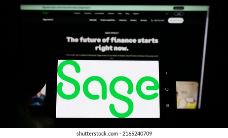 Stuttgart, Germany - 05-29-2022: Person holding smartphone with logo of British software company The Sage Group plc on screen in front of website. Focus on phone display. Unmodified photo.