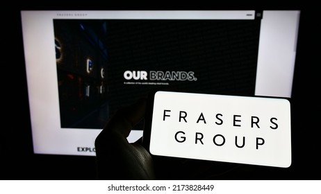 Stuttgart, Germany - 06-04-2022: Person Holding Mobile Phone With Logo Of British Retail Company Frasers Group Plc On Screen In Front Of Business Webpage. Focus On Phone Display. Unmodified Photo.