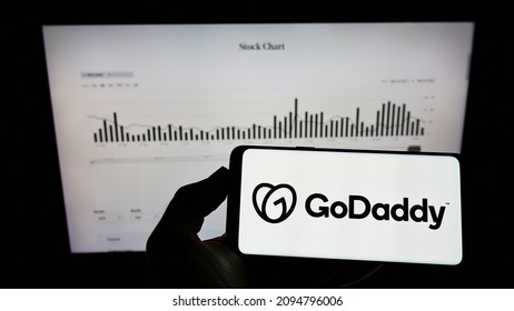 Stuttgart, Germany - 12-11-2021: Person holding mobile phone with logo of American web hosting company GoDaddy Inc. on screen in front of web page. Focus on phone display. Unmodified photo.