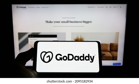 Stuttgart, Germany - 12-11-2021: Person holding smartphone with logo of US web hosting company GoDaddy Inc. on screen in front of website. Focus on phone display. Unmodified photo.