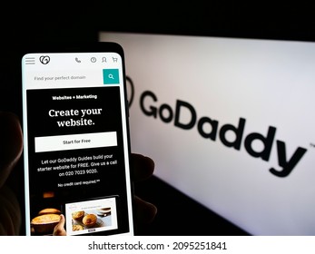 Stuttgart, Germany - 12-11-2021: Person holding smartphone with website of American web hosting company GoDaddy Inc. on screen in front of logo. Focus on center of phone display. Unmodified photo.
