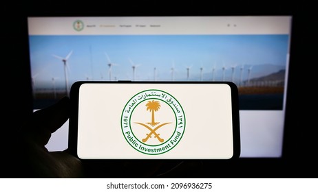 Stuttgart, Germany - 12-18-2021: Person Holding Cellphone With Logo Of Saudi Arabian Public Investment Fund (PIF) On Screen In Front Of Business Webpage. Focus On Phone Display. Unmodified Photo.