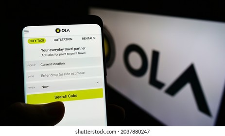 STUTTGART, GERMANY - Jul 12, 2021: Person holding smartphone with website of Indian company Ola Cabs on screen in front of logo  Focus on center of phone display 