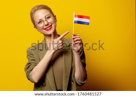 Style blonde woman in jacket with Dutch flag on yellow background