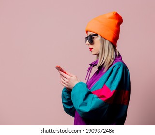 Style Girl In 80s Sportsuit And Sunglasses Hold Mobile Phone On Pink Background