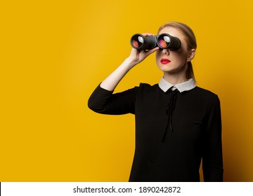 Style woman in black formal clothes with binocular on yellow background