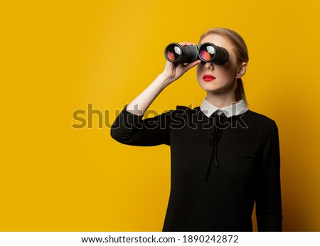 Style woman in black formal clothes with binocular on yellow background