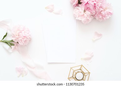 Styled feminine top view.on white background with wedding card, pink peonies petals, candle