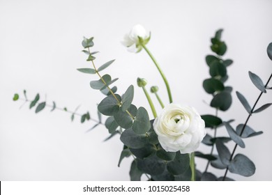 Styled photo of ranunculus and eucalyptus bouquet on pale background. Floral minimal composition