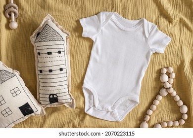 Styled Stock Photo Of Clear White Baby Onesie With Scandinavian Stitched Pillow In The Shape Of A House And Wooden Toys On Yellow Napkin For Creating Mockup For Presentation Kids Sublimation Design