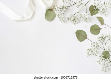 Styled stock photo. Feminine wedding desktop mockup with baby's breath Gypsophila flowers, dry green eucalyptus leaves, satin ribbon and white background. Empty space. Top view. Picture for blog. - Shutterstock ID 1006715578