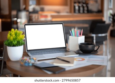 A styled workspace in a cafe setting featuring an open laptop mockup, colorful pencils, coffee cup, notebook, and plant for creative business use.