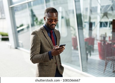 Stylish African American black businessman works on his smartphone standing before a modern glass building outside - Shutterstock ID 1081066667