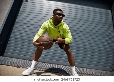 A stylish African American man in a green hoodie holding a basketball. - Powered by Shutterstock