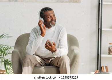 stylish african american man sitting in armchair and listening music in headphones
