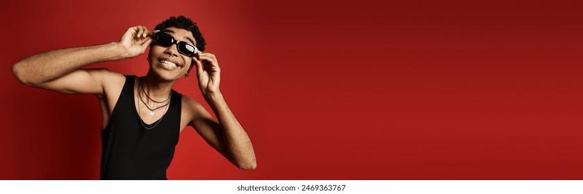 A stylish African American man in sunglasses and a black tank top striking a pose on a vibrant red background. - Powered by Shutterstock