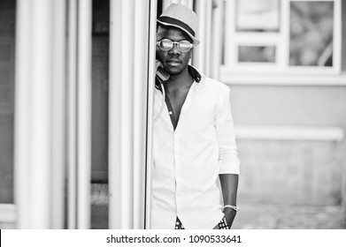 Stylish African American Man In White Shirt And Colored Pants With Hat And Glasses Posed Outdoor At Telephone Booth. Black Fashionable Model Boy.