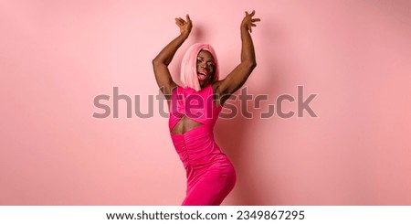 Stylish African transgender person looks happy while posing on a pink background.