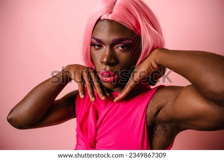 Stylish African transgender person in pink wig and clothes posing in a studio.