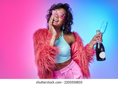 Stylish African woman holding bottle and sparkling wine   smiling against colorful background