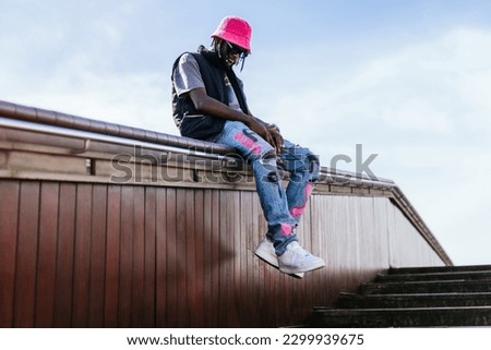 A stylish African youth sits on a wooden stairway runway, dressed in modern casual wear on a sunny day