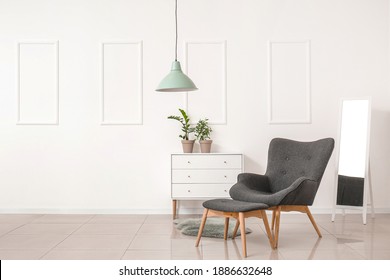 Stylish armchair and ottoman with chest of drawers and mirror in room